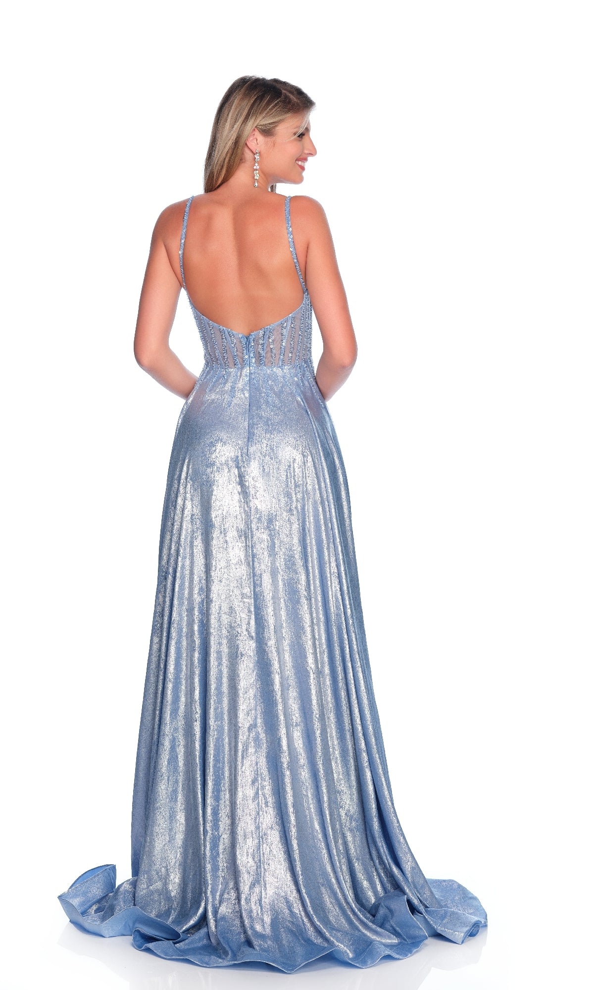 A woman stands with her back to the camera, wearing the Dave & Johnny 12180 Metallic Blue Prom Dress—floor-length, sleeveless, with a low back and sheer bodice.